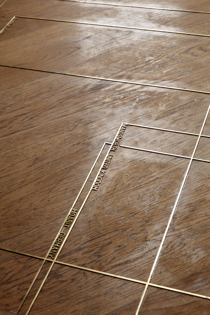 Outlines of prison cells in brass on wooden floor.