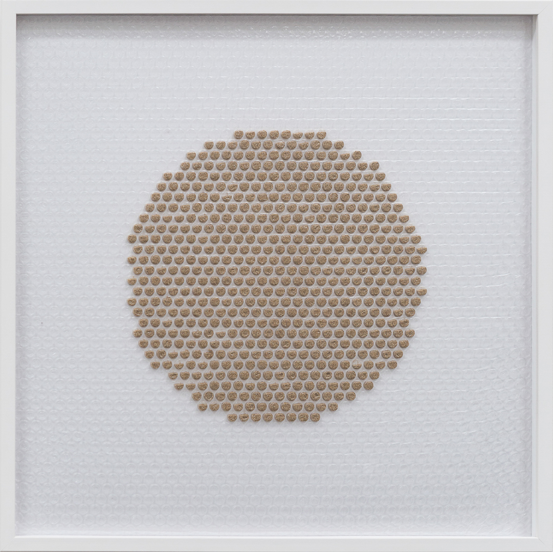 A circle made by injecting brown paint in some of the bubbles of a bubble wrap. Framed by white colored wood