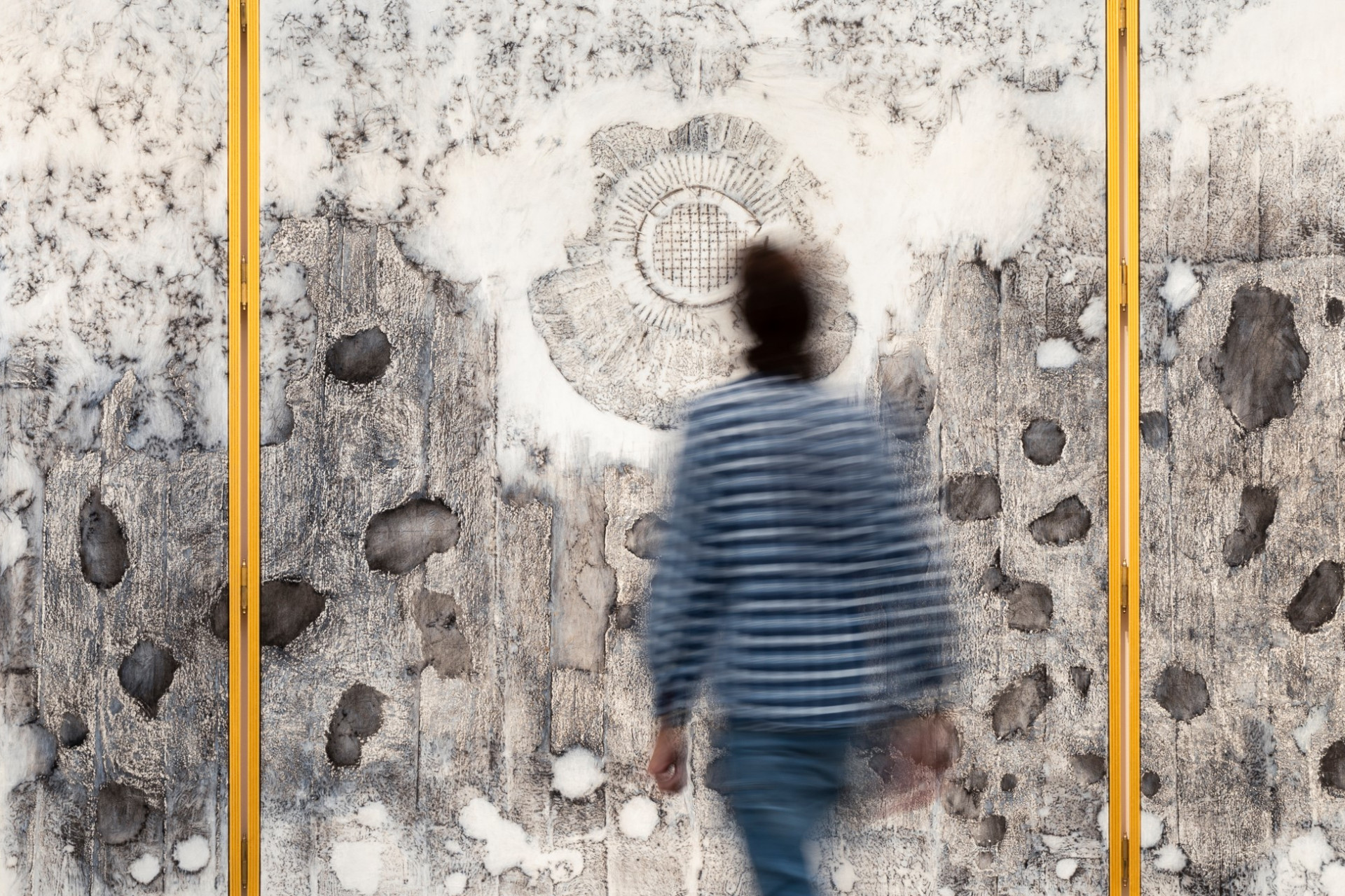 Photo of Nadia Kaabi-Linke's painting The Altarpiece showing a man walking towards the canvasses with transfer prints of wall damages.