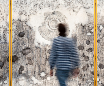 Photo of Nadia Kaabi-Linke's painting The Altarpiece showing a man walking towards the canvasses with transfer prints of wall damages.