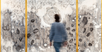 Photo of Nadia Kaabi-Linke's painting The Altarpiece showing a man walking towards the canvasses with transfer prints of wall damages.