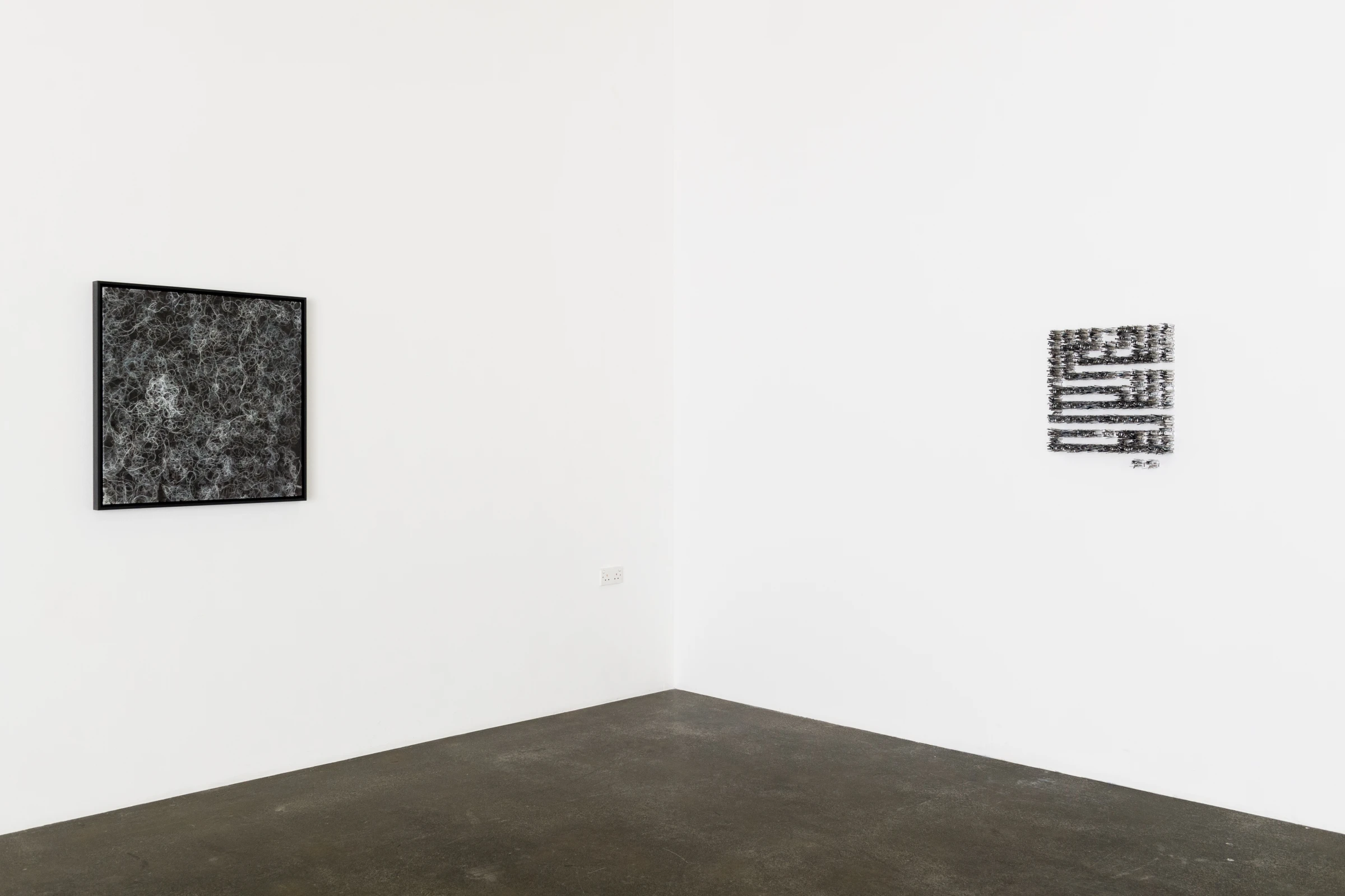 Two artworks hanging in the corner of an gallery wall.