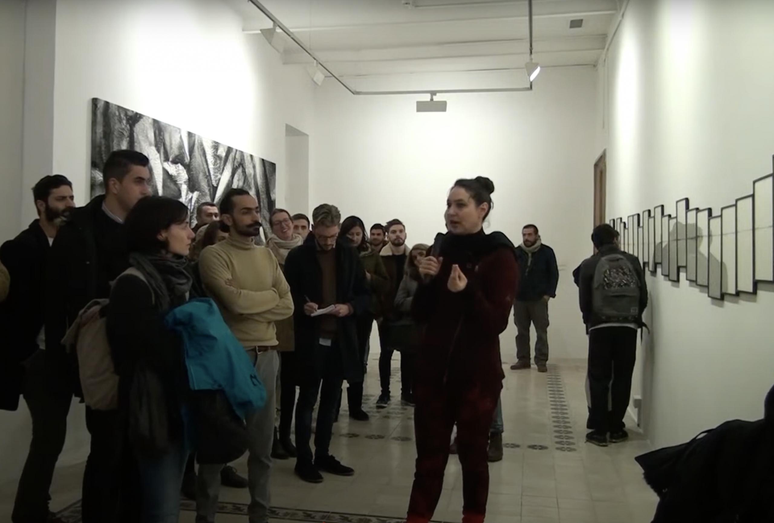 A group of people standing around a woman explaining the works on the wall.