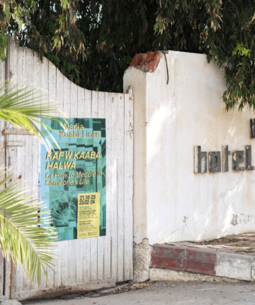 A white, wooden gate, that was once the entrance to the Hotel Megara Gammarth, is now holding the poster about an exhibition. Nadia Kaabi-Linke Kaf w Kaaba Halwa, ONS