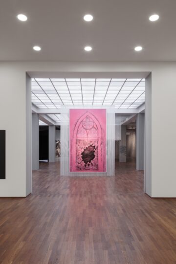 Black squares hanging on the walls of an exhibition space, in the background, another room, with a big pink painting. Nadia Kaabi-Linke Seeing Without Light