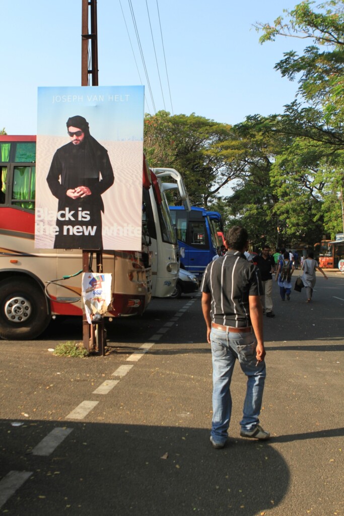 A man walks along a busy street past a poster depicting a man in the desert