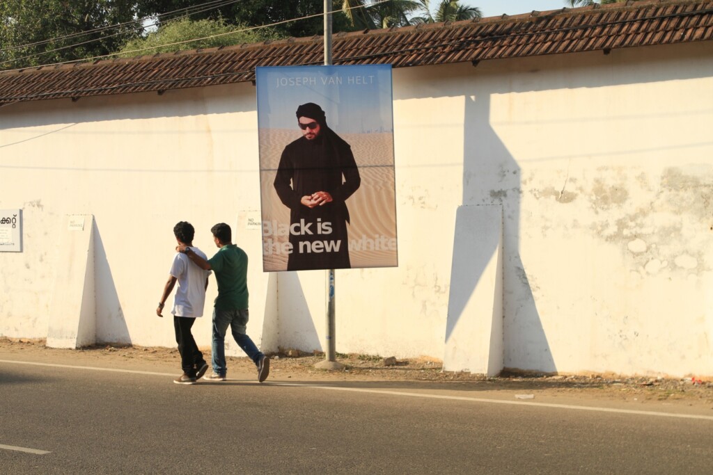 Two boys walk in front of a large poster with a photo of a man in the desert
