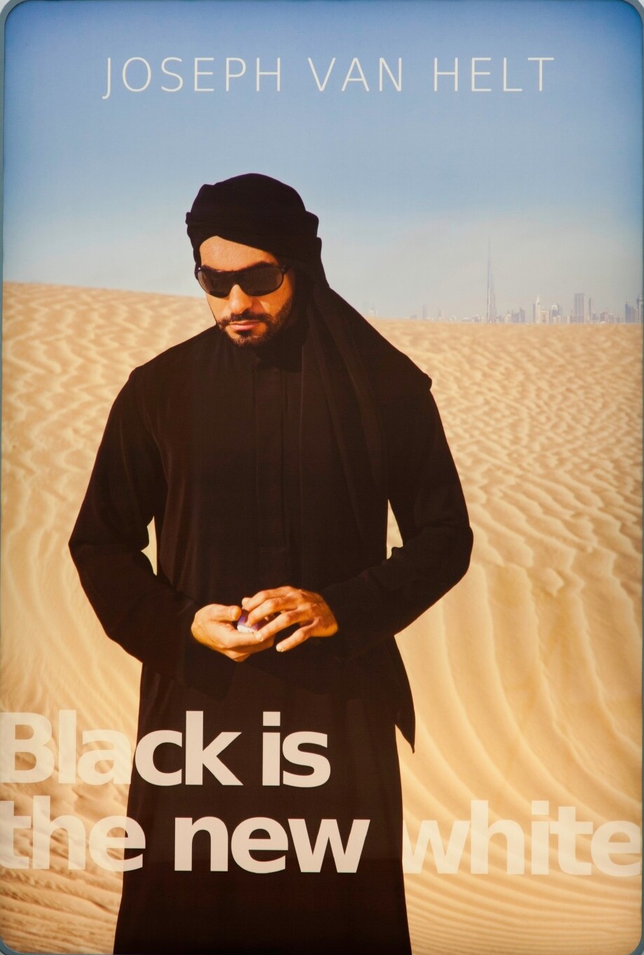 A man stands in the desert, with Dubai in the background. The title reads "Black is the new white."