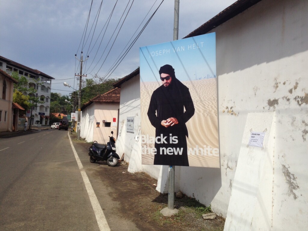 View of a street surrounded by houses. In the foreground, a large poster depicting a man in the desert