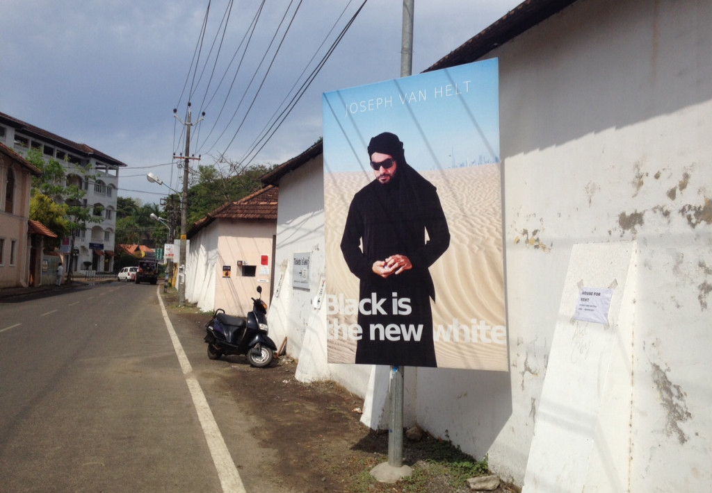 View of a street surrounded by houses. In the foreground, a large poster depicting a man in the desert