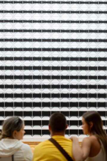 Tree people sitting in front of an artwork, photographed from behind.