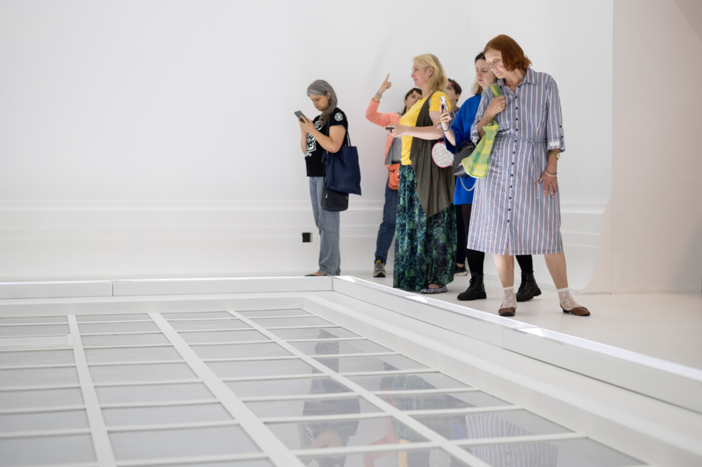 A group of people looking at an art installation made of transparent acrylic squares on the ground.