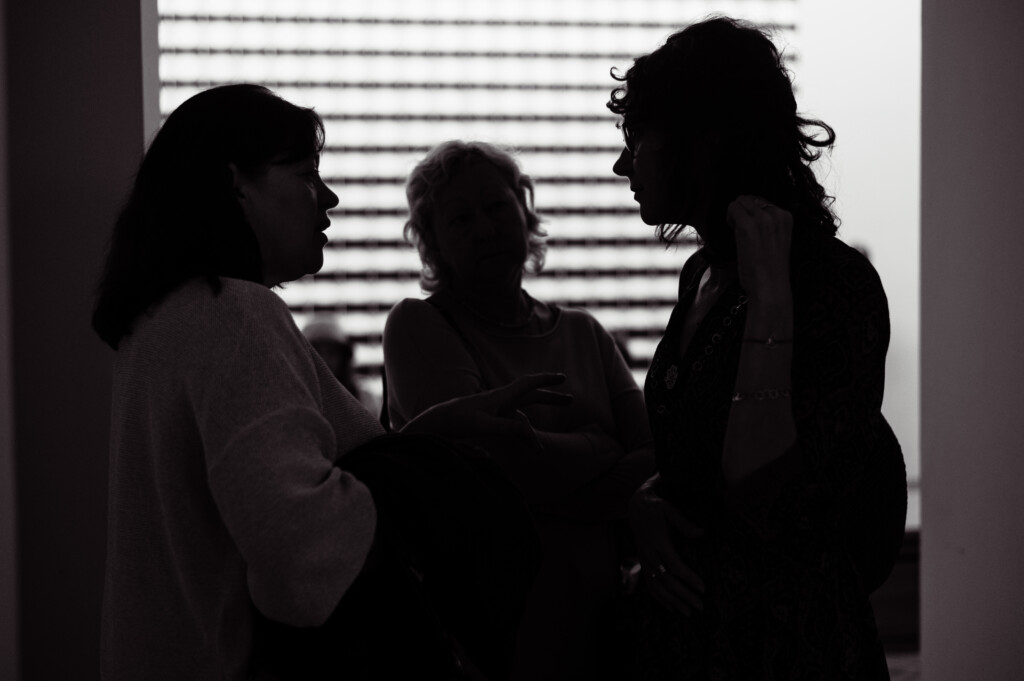 The silhouettes of visitors in an exhibition space talking to each other.