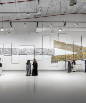 Visitors of an exhibition standing in front of the depiction of a big arrow. Nadia Kaabi-Linke, E Pluribus Unum.