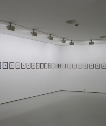 Many small framed images hanging in line on an exhibition wall. Nadia Kaabi-Linke, Faces.