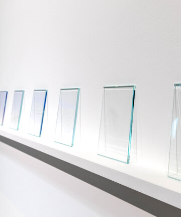 The wall of an exhibition space. A row of glass squares sit on a white shelf. Nadia Kaabi-Linke Impunities – London