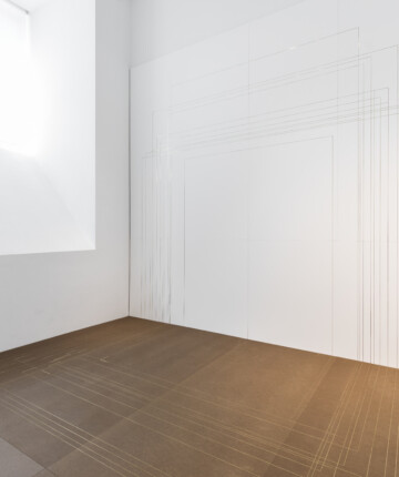 Exhibition space with gold lines crossing a brown mdf panel. The lines go all the way up the white wall. Creating multiple different sized squares. Nadia Kaabi-Linke, Modulor I.
