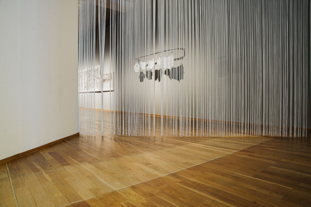 An exhibition space separated by a curtain of white threats.