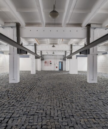 A big industrial space covered in cobblestones. on the wall the negative spaces of the cobblestones on the floor. Nadia Kaabi-Linke, Remont / Ремонт.