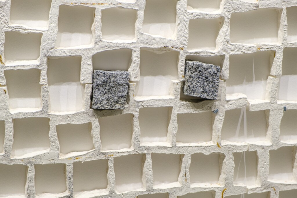 A white wall with holes in the form of cobblestones. Two holes still have the cobblestones inside.