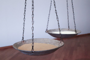 A vintage balance scale with two shallow bowls: one with light brown sand and the other with salt, hanging from chains. / Salt and Sand, Exhibition view, Seeing without Light, Hamburger Bahnhof, Berlin, 2023, Nadia Kaabi-Linke