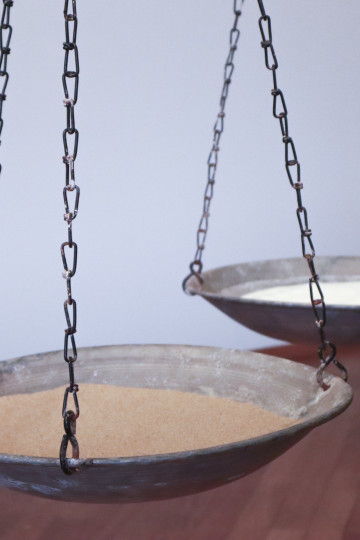A vintage balance scale with two shallow bowls: one with light brown sand and the other with salt, hanging from chains. / Salt and Sand, Exhibition view, Seeing without Light, Hamburger Bahnhof, Berlin, 2023, Nadia Kaabi-Linke