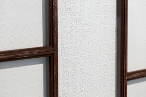 Detail of glass windows with the shadow of a maschrabiyya pattern, framed by a dark wood.