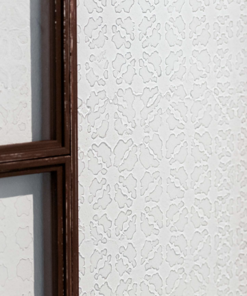 Detail of glass windows with the shadow of a maschrabiyya pattern, framed by a dark wood. Nadia Kaabi-Linke, Amina's Tears.