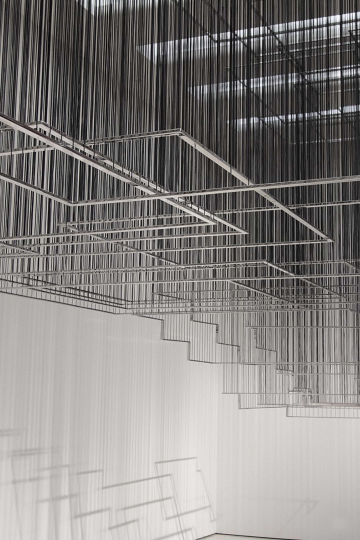 Metal rods, forming different sized squares, hanging from the ceiling by thin wires. Nadia Kaabi-Linke, Flying Carpets.