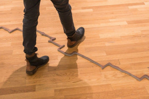 Someone, only visible from the knees down, stepping over an uneven brown line laying on a wooden floor.