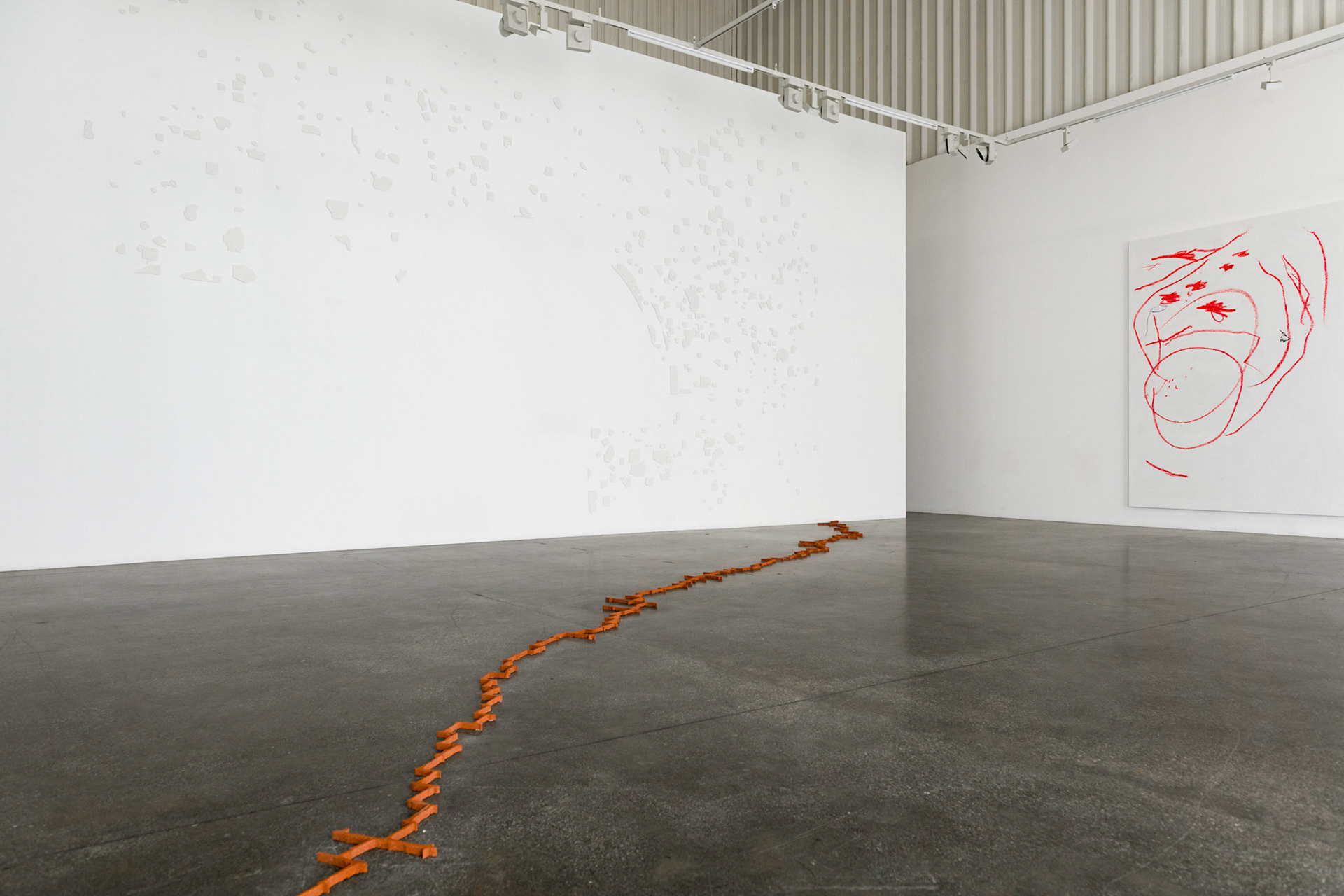View of an exhibition space with a painting hanging on the wall and a zick zack line made of an earthy material laying on the concrete floor.