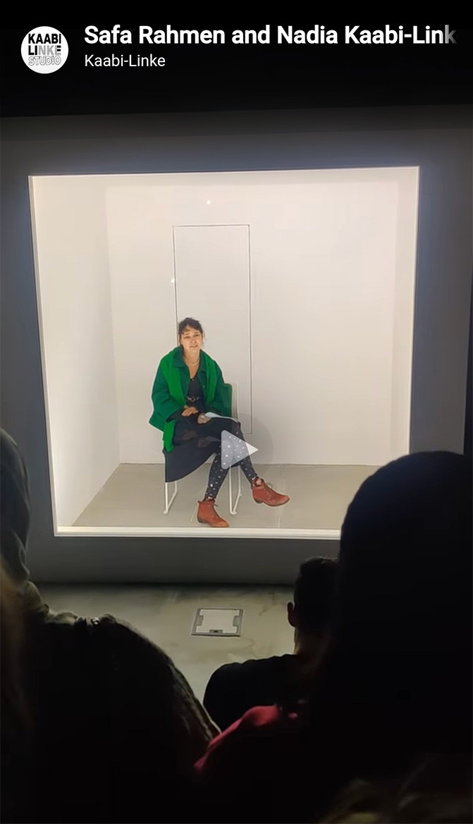 Performance artwork with artist Nadia Kaabi-Linke sitting inside a lit cube in front of the audience.