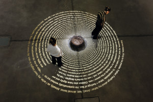 A spiral with text on the ground, and a nest with barbwire and hair. Twp persons reading. Exhibition view of Tatort / Crime Scene exhibition by Nadia Kaabi-Linke in 2010.