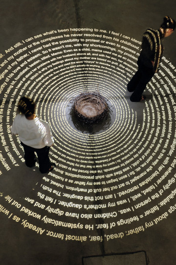 A spiral with text on the ground, and a nest with barbwire and hair. Twp persons reading. Exhibition view of Tatort / Crime Scene exhibition by Nadia Kaabi-Linke in 2010.