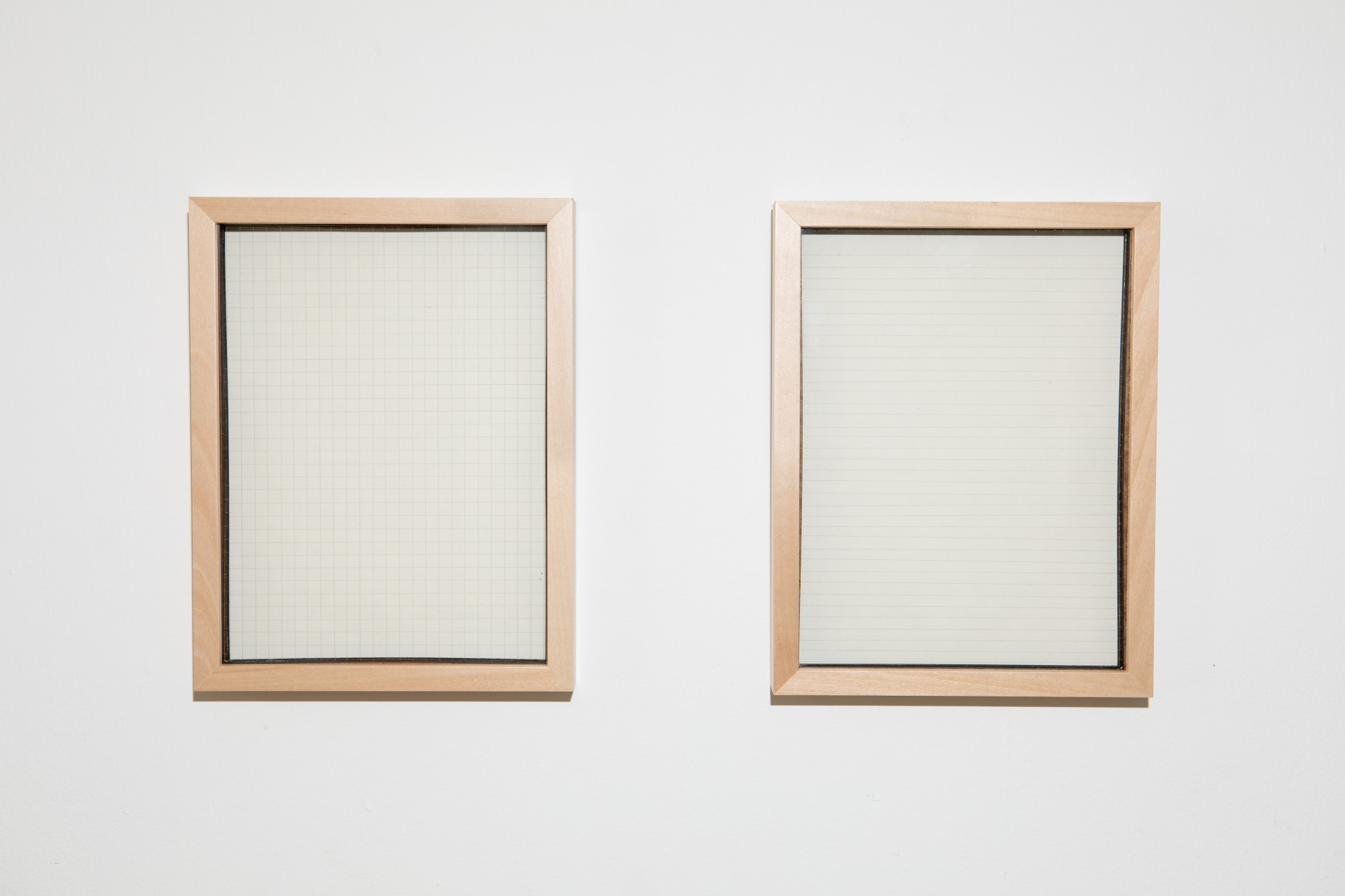 Two object frames showing squares and lines on paper hanging on a wall.