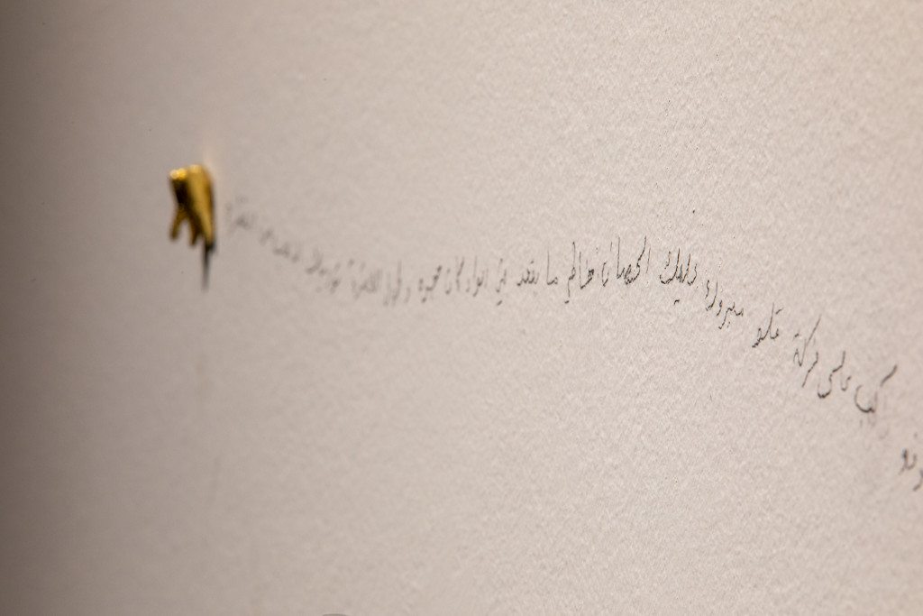 A line of words written in pencil on a white wall. At the end of the text, a gold tooth is stuck to the wall.