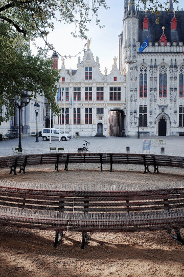 In a public space, benches are placed to create a circle. The benches are covered in bird spices. Nadia Kaabi-Linke, Inner Circle.
