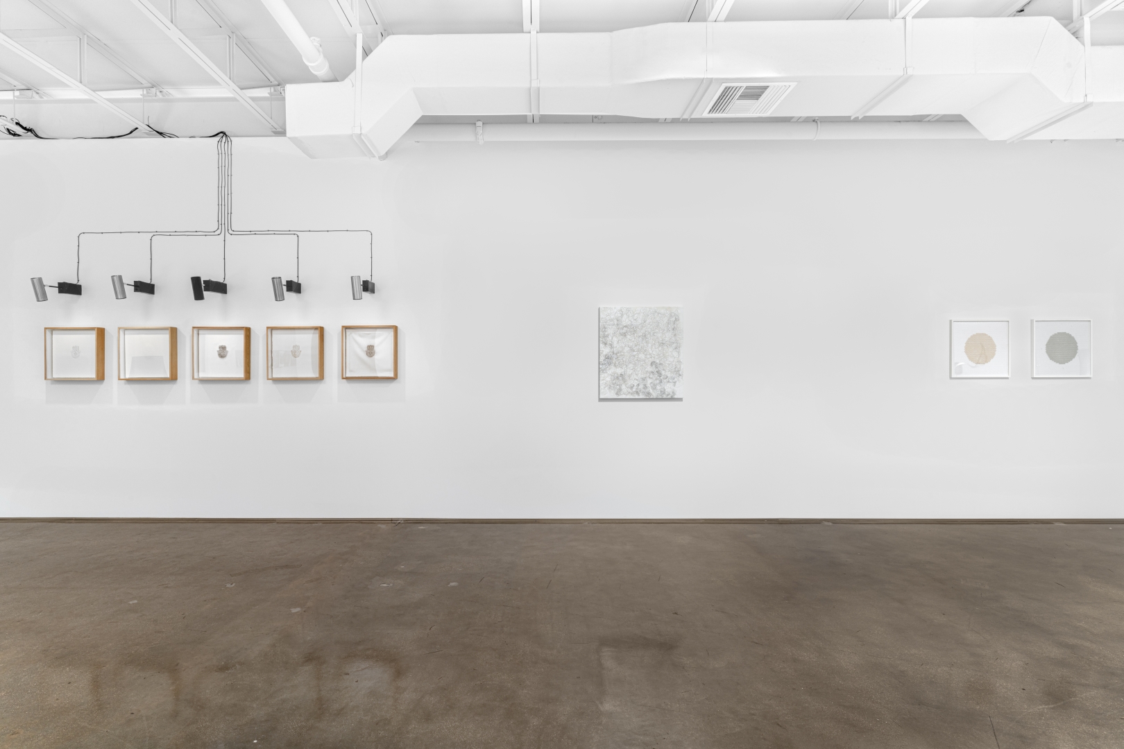 White and bright gallery with an installation, painting and two objects hanging on one wall.