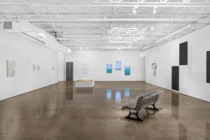 White and bright gallery space with industrial ceiling and various artworks.