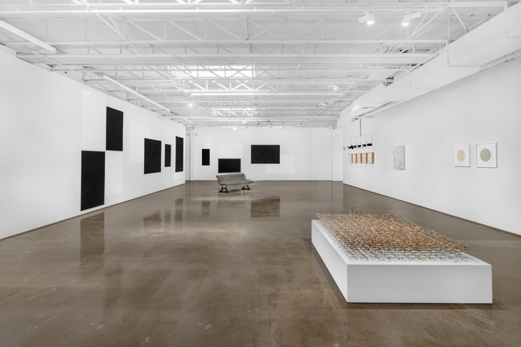 White gallery with industrial ceiling and various artworks.