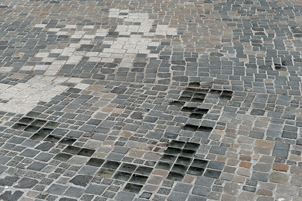 Public square with paving stones, with some of the missing, leaving an empty form.