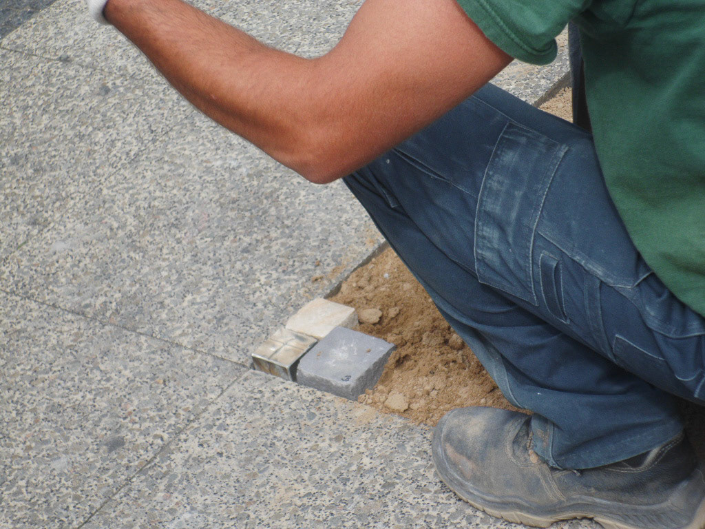 A space in the ground is being filled by paving stones of different size and color.