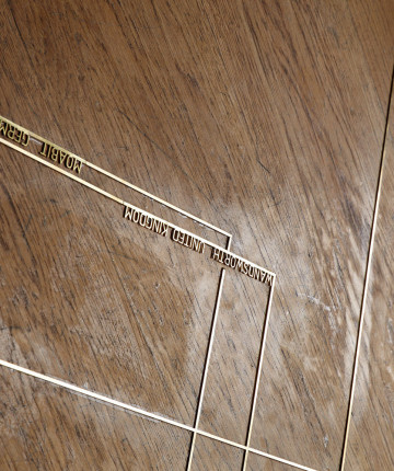 Brass lining with the name of prison location on a wood floor.
