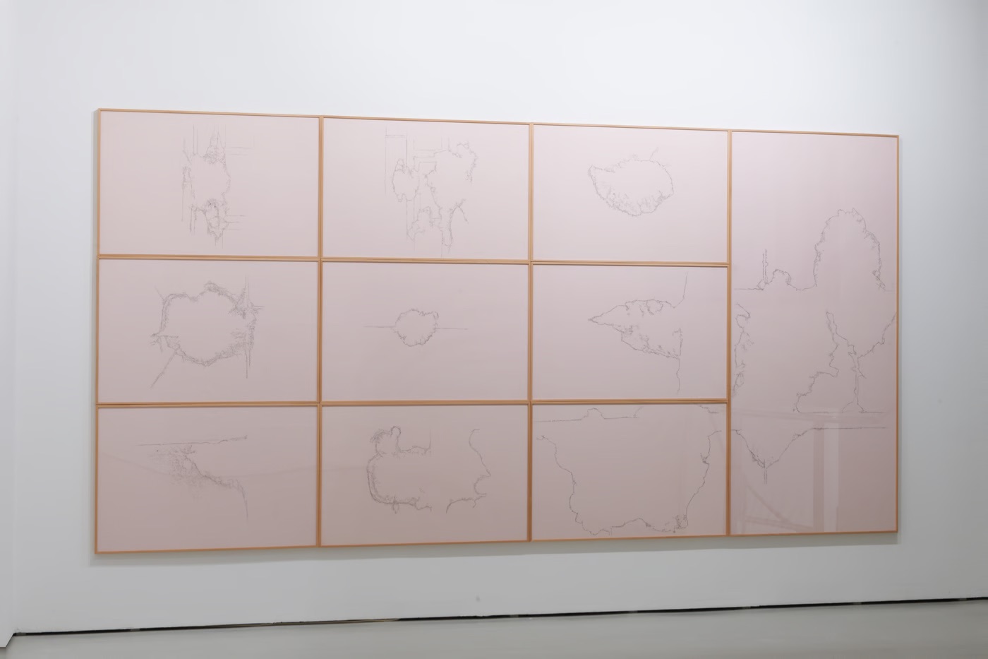 10 framed drawings on graph paper, hung right next to each other. The drawings are exact outlines of bullet destructions in walls.