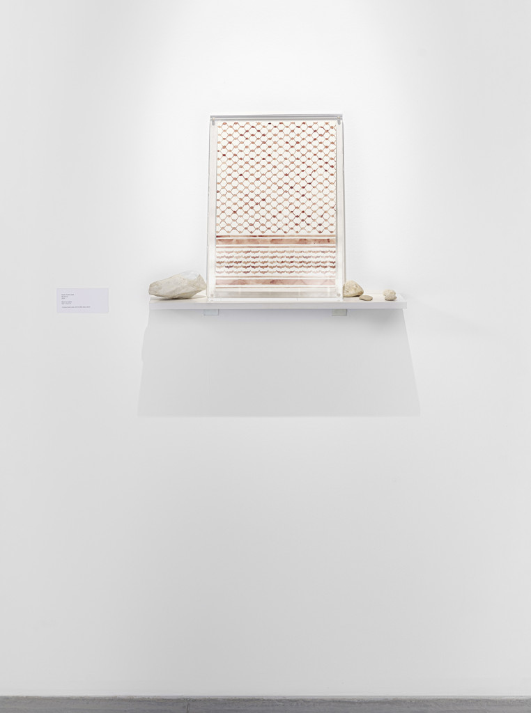 Behind glass, mounted to the white wall with screws, hangs a drawing with the patterns of a keffiyeh painted in blood.
