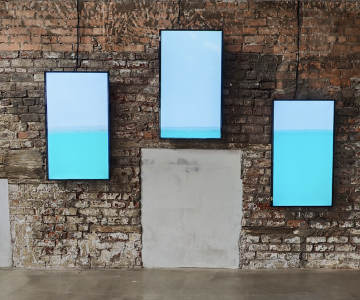 A video of the sea divided on three vertical screens hanging on a brick stone wall. Nadia Kaabi-Linke Under Sea Heart Beats