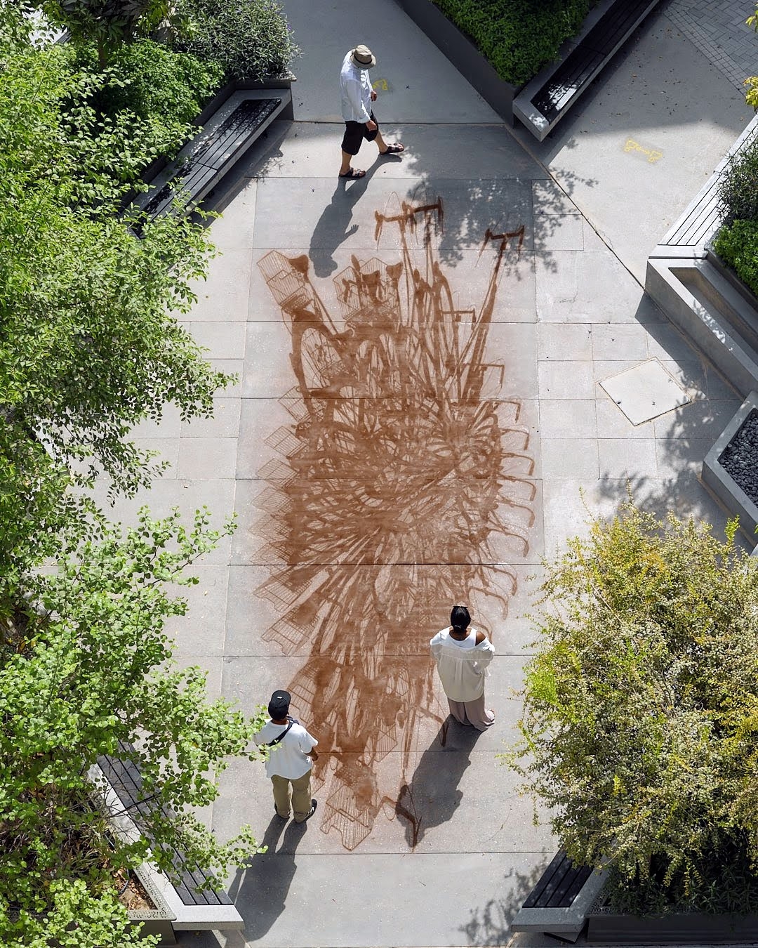 Bird's eye view of two people walking on a rusty abstract image of steel inlayed in concrete.
