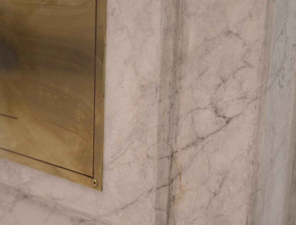 Nadia Kaabi-Linke, To the Olives, 2026. Detail of the veined white marble plinth and the edge of the brass label fixed with a screw.